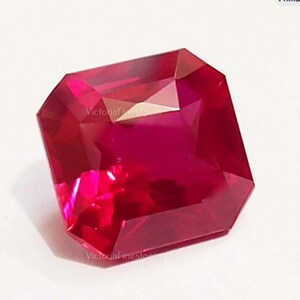 Op de afbeelding: Een gefacetteerde, rechthoekig geslepen robijn edelsteen. De edelsteen heeft een diepe, verzadigde rode kleur met meerdere facetten die licht reflecteren. De tekst "VictoriaFinesgems" is zichtbaar op de edelsteen.