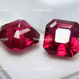 May include: Two faceted, deep red gemstones. One is a modified hexagonal shape, the other is an emerald cut. The gems are displayed on a light background. The text "ParigemsGifts" is visible in the corners.