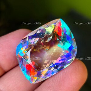 May include: A large, faceted gemstone with a vibrant display of colors including red, blue, green, and yellow. The gem is held in a hand, showcasing its intricate cuts and reflective surfaces. The gemstone is a focal point, with a dark background.