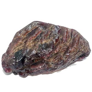 May include: A rough, uncut gemstone with a dark, mottled appearance. The stone displays a mix of deep burgundy, brown, and hints of lighter colors. The surface has a textured, uneven quality, suggesting a natural, unpolished state.