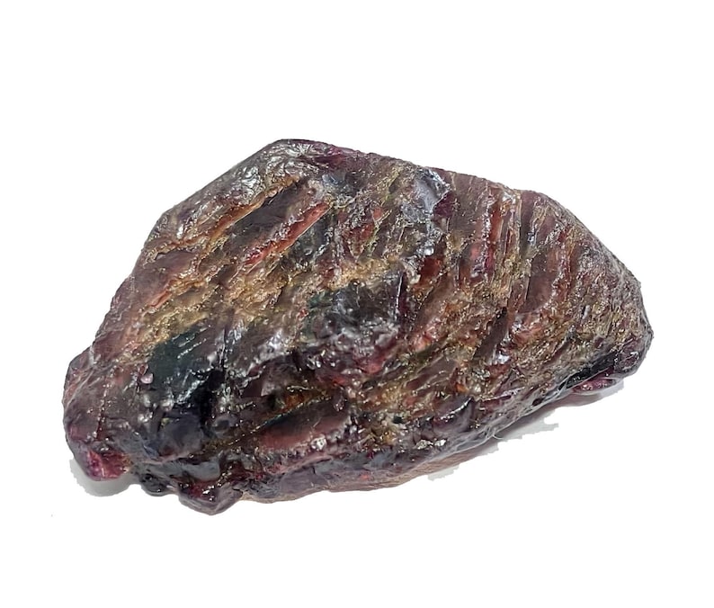 May include: A rough, uncut gemstone with a dark, mottled appearance. The stone displays a mix of deep burgundy, brown, and hints of lighter colors. The surface has a textured, uneven quality, suggesting a natural, unpolished state.