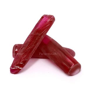 Peut inclure: Trois pierres précieuses de rubis polies et allongées. Les pierres précieuses sont d'un rouge profond avec une finition brillante. Les pierres sont disposées en composition triangulaire sur fond blanc.