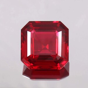 Könnte beinhalten: Ein quadratisch geschliffener Edelstein mit einer leuchtend tiefroten Farbe und einer facettierten Oberfläche. Der Stein zeichnet sich durch eine klare, transparente Qualität mit scharfen, geometrischen Kanten und symmetrischen Facetten aus.