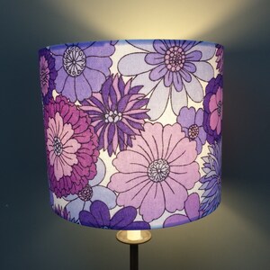 May include: A purple and white floral lampshade with a retro design. The lampshade features a variety of flowers in different shades of purple and white.