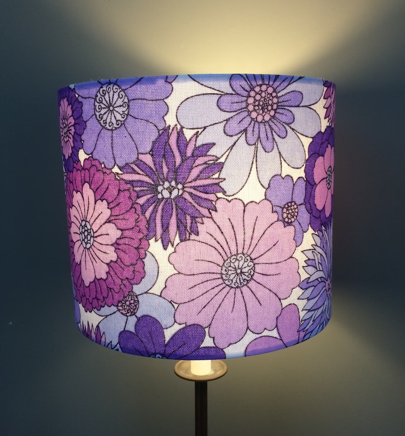 May include: A purple and white floral lampshade with a retro design. The lampshade features a variety of flowers in different shades of purple and white.