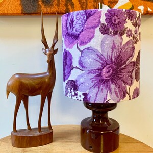 May include: A table lamp with a purple floral patterned lampshade and a dark brown ceramic base. A wooden deer figurine is in the foreground.