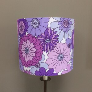 May include: A purple and white floral lampshade with a large, bold floral pattern. The lampshade is made of fabric and has a white background with purple flowers.