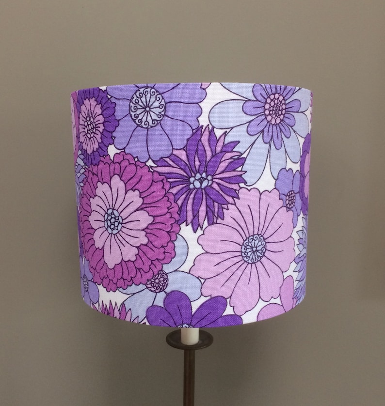 May include: A purple and white floral lampshade with a large, bold floral pattern. The lampshade is made of fabric and has a white background with purple flowers.