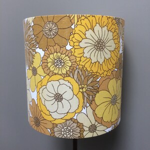 May include: A yellow and brown floral lampshade with a retro design. The lampshade features a variety of flower shapes and sizes, with a white background.
