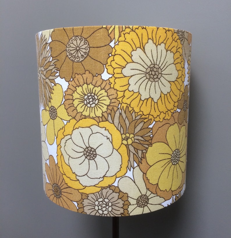 May include: A yellow and brown floral lampshade with a retro design. The lampshade features a variety of flower shapes and sizes, with a white background.