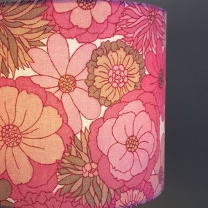 May include: A pink and brown floral lampshade with a retro design. The lampshade features a variety of flowers in different sizes and shapes.