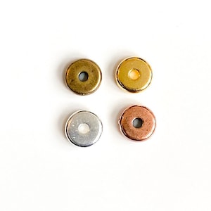 May include: Four round metal beads in different colors: gold, brass, silver, and copper. Each bead has a hole in the center.