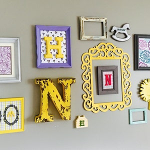 May include: A wall gallery featuring a variety of framed artwork, including a paisley pattern, a checkered pattern, and a floral design. The gallery also includes wooden letters spelling out the word "HUNTER" in yellow and a small wooden rocking horse.