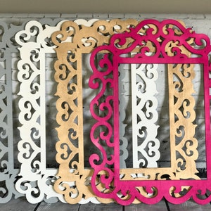 K&ouml;nnte beinhalten: Vier dekorative Bilderrahmen aus Holz mit verzierten Designs. Die Rahmen sind in verschiedenen Farben: Grau, Wei&szlig;, Gold und Pink.