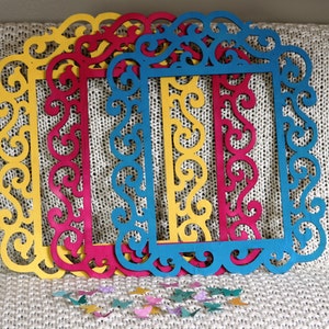 May include: Four decorative picture frames with intricate cut-out designs. The frames are layered on top of each other and are painted in shades of yellow, red, blue, and teal.