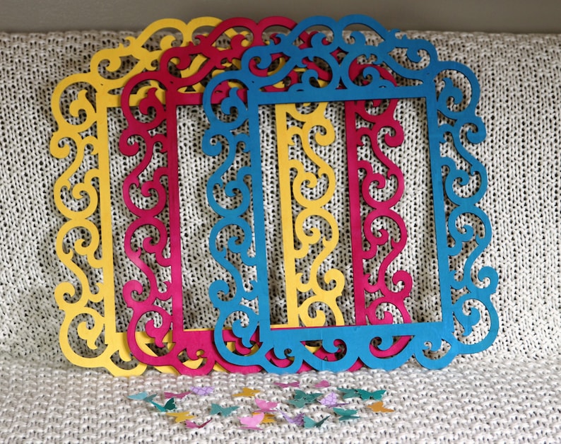 May include: Four decorative picture frames with intricate cut-out designs. The frames are layered on top of each other and are painted in shades of yellow, red, blue, and teal.