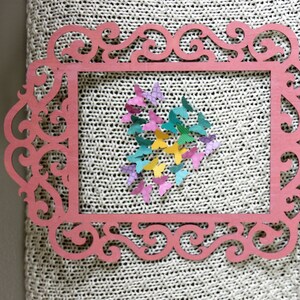 May include: A pink wooden frame with an ornate design, featuring a heart shape made of colorful paper butterflies.