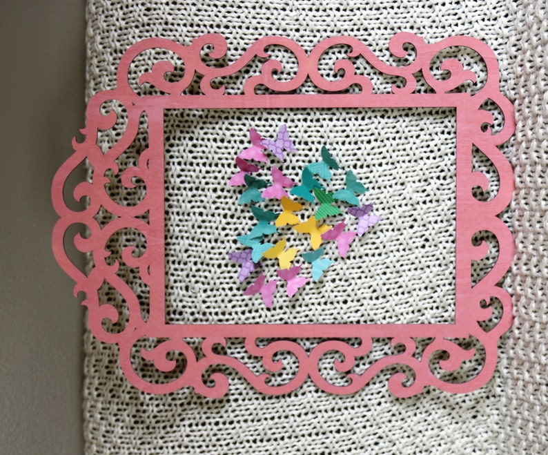 May include: A pink wooden frame with an ornate design, featuring a heart shape made of colorful paper butterflies.