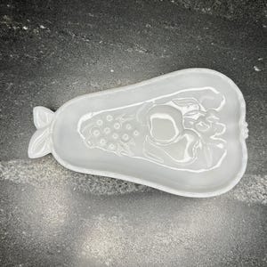 Könnte beinhalten: Weiße Keramik-Schale in Birnenform mit einem erhabenen Design aus Trauben und einer Birne. Die Schale ist perfekt zum Servieren von Snacks oder Vorspeisen.