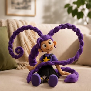 May include: A plush doll with tan skin, large eyes, and a small smile. The doll has long, thick, purple yarn hair styled into two large, arched braids. It wears a purple short-sleeved shirt with a yellow star, a black skirt, and black shoes.