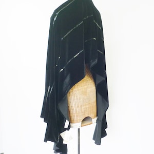 May include: A black velvet shawl with diagonal rows of sequins. The shawl has a flowing design with a satin trim and is draped over a wicker form. The garment is displayed against a white background.