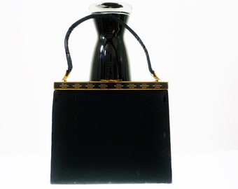 Könnte beinhalten: Eine schwarze Samt-Handtasche mit einem goldenen Verschluss und einem schwarzen Lederriemen.