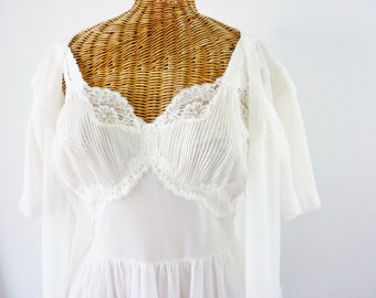 May include: White vintage lingerie set featuring a pleated bodice with lace trim and a flowing skirt. The set includes a matching sheer robe with short sleeves. The lingerie is displayed on a wicker mannequin.