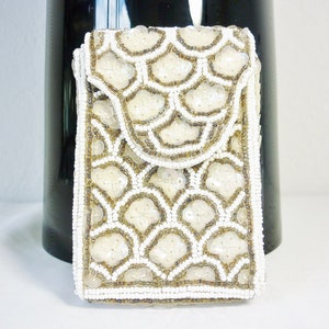 May include: Ivory beaded clutch with a scalloped flap. The rectangular bag features a repeating pattern of white and gold-toned beads. The flap and edges are also beaded. The bag is set against a dark background.