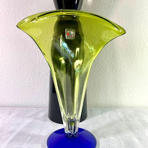 May include: A modern art glass vase with a flared, chartreuse-colored top and a deep blue base. The vase has a tall, black cylindrical support and a clear, slender neck. A small, square sticker is visible on the front.