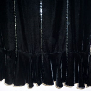May include: Black velvet dress with vertical rows of sequins. The dress features a flared hemline. The fabric has a soft, luxurious appearance. The dress is suitable for formal occasions.