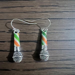 May include: A pair of silver-toned microphone earrings. The microphone bodies have a textured design, and the handles are striped with green, orange, and white. The earrings have a hook closure.