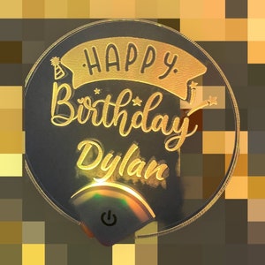 May include: A black circular light-up sign with a gold inscription that reads "Happy Birthday Dylan". The sign has a small on/off switch on the bottom.