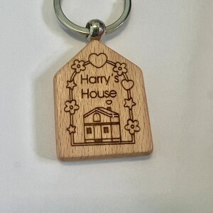 May include: Wooden house-shaped keychain with a silver key ring. The keychain is engraved with the text "Harry's House" and features a small house illustration with a heart above it.