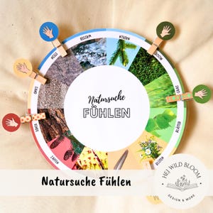 Könnte beinhalten: Ein kreisförmiges Lernspiel mit dem Text "Natursuche Fühlen" und verschiedenen Naturelementen wie Wasser, Stein und Sand. Jeder Abschnitt wird von einer Holzklammer mit einer Handillustration gehalten. Das Spiel ist für taktile Erkundung konzipiert.