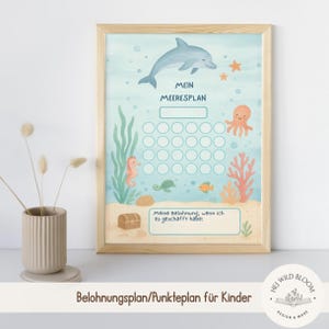 May include: A framed watercolor print featuring an underwater scene with a dolphin, octopus, seahorse, and other sea creatures. The print includes the text "MEIN MEERESPLAN" and a reward chart for children. The frame is made of light-colored wood.