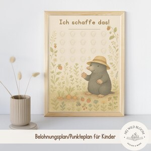 May include: A framed print featuring a cartoon mole wearing a straw hat, set in a garden scene with carrots and strawberries. The text "Ich schaffe das!" is at the top. The print is in a light wood frame.