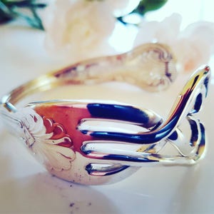 Op de afbeelding: Een zilveren vorkarmband met een decoratief ontwerp. De armband is gemaakt van twee in elkaar verweven vorken.