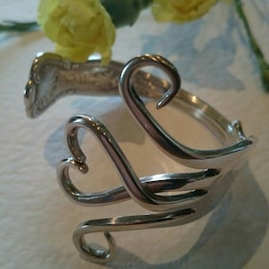 Puede incluir: Un brazalete de plata hecho a partir de un tenedor reutilizado, con los dientes doblados en forma de corazón.