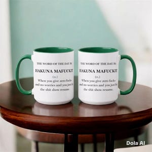 Op de afbeelding: Twee witte keramische mokken met donkergroene binnenkant en oren. Elke mok is voorzien van zwarte tekst: THE WORD OF THE DAY IS: HAKUNA MAFUCKIT (n.) When you give zero fucks and no worries and you just let the shit show resume.