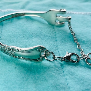 May include: A silver bracelet made from a vintage fork with a heart charm attached to a chain.