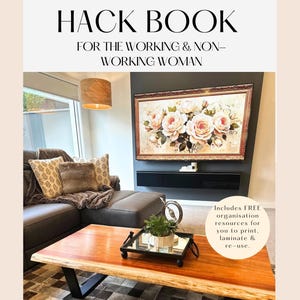 Könnte beinhalten: Ein Buch mit dem Titel "The Housewife Hack Book" für berufstätige und nicht berufstätige Frauen. Der Buchumschlag zeigt ein Wohnzimmer-Interieur mit einer Couch, einem Couchtisch und einem gerahmten Rosenbild. Der Text "By Amira Essam" befindet sich am unteren Rand des Umschlags. Das Buch enthält kostenlose Organisationsressourcen zum Ausdrucken, Laminieren und Wiederverwenden.