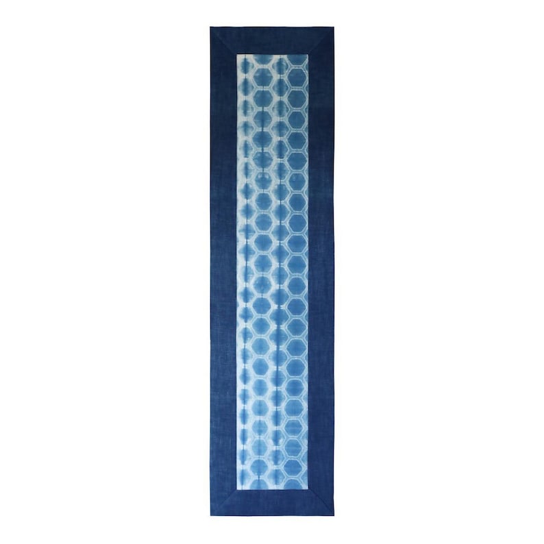 May include: A rectangular indigo blue table runner with a white and blue honeycomb pattern in the center. The runner has a dark blue border. The design is symmetrical and the background is white.