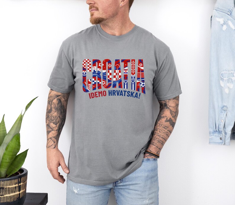 May include: A gray t-shirt with the word "CROATIA" in a colorful, patterned design, with the text "IDEMO HRVATSKA!" below. The shirt is short-sleeved and appears to be made of a soft material.