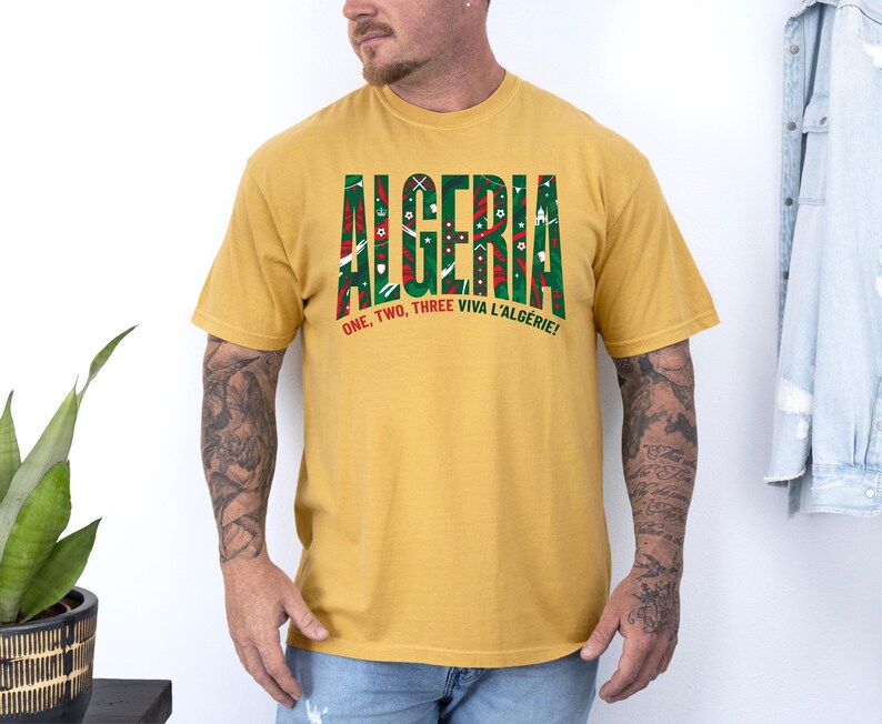 K&ouml;nnte beinhalten: Senfgelbes T-Shirt mit dem Wort "ALGERIA" in gro&szlig;en, gr&uuml;n und rot gemusterten Buchstaben. Darunter steht der Text "ONE, TWO, THREE VIVA L'ALG&Eacute;RIE!"
