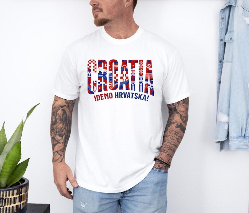 May include: White t-shirt with the word "CROATIA" in red, white, and blue, with various Croatian flag-themed designs within the letters. Below the word is the text "IDEMO HRVATSKA!"