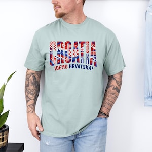 May include: A light green t-shirt with the word "CROATIA" in red, white, and blue, with various Croatian flag-inspired designs. Below the word is the text "IDEMO HRVATSKA!"