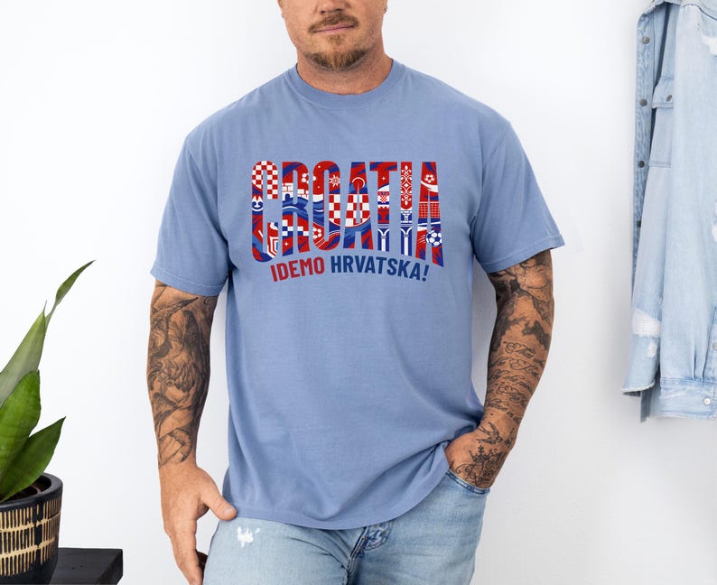 May include: A light blue t-shirt with the word "CROATIA" in a red, white, and blue design, with the text "IDEMO HRVATSKA!" below. The shirt is made of a soft material.