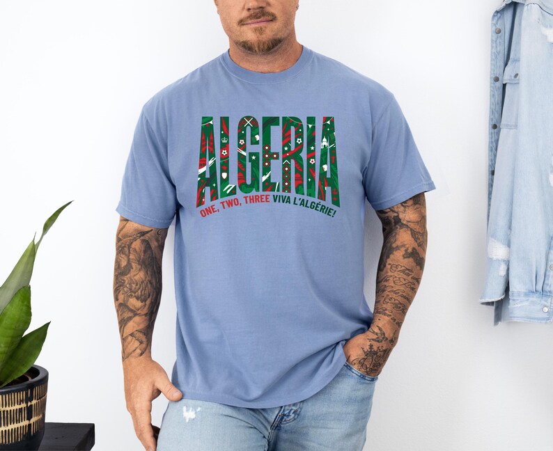 K&ouml;nnte beinhalten: Ein hellblaues T-Shirt mit dem Wort "ALGERIA" in gr&uuml;nen und roten Blockbuchstaben. Das T-Shirt hat auch den Text "ONE, TWO, THREE VIVA L'ALG&Eacute;RIE!" in Rot. Das T-Shirt ist aus weichem Material.