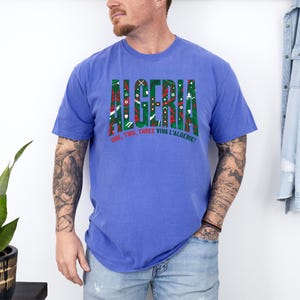 K&ouml;nnte beinhalten: Ein blaues T-Shirt mit dem Wort "ALGERIA" in einem gr&uuml;n-roten Muster. Darunter steht der Text "ONE, TWO, THREE VIVA L'ALG&Eacute;RIE!"