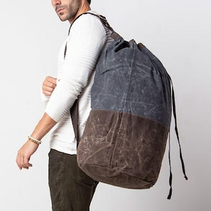 May include: A large, two-tone backpack with a drawstring closure. The top portion is a dark blue-gray, and the bottom is a deep brown. The bag is carried over the shoulder with black straps.